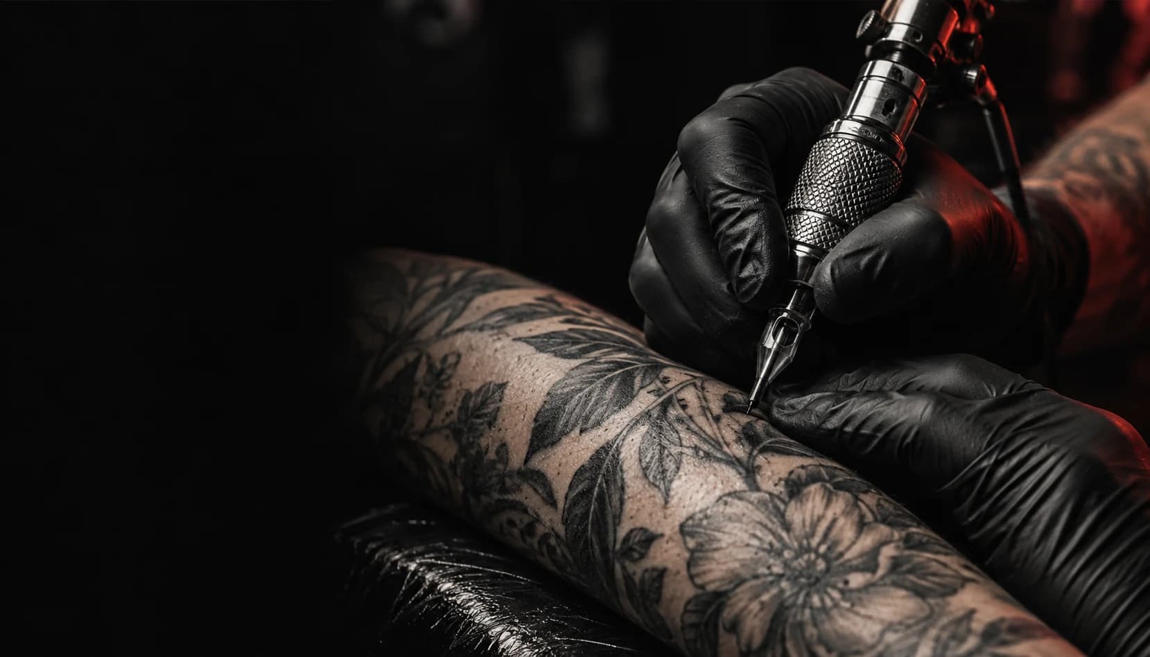 Black-gloved tattoo artist working on an intricate botanical tattoo